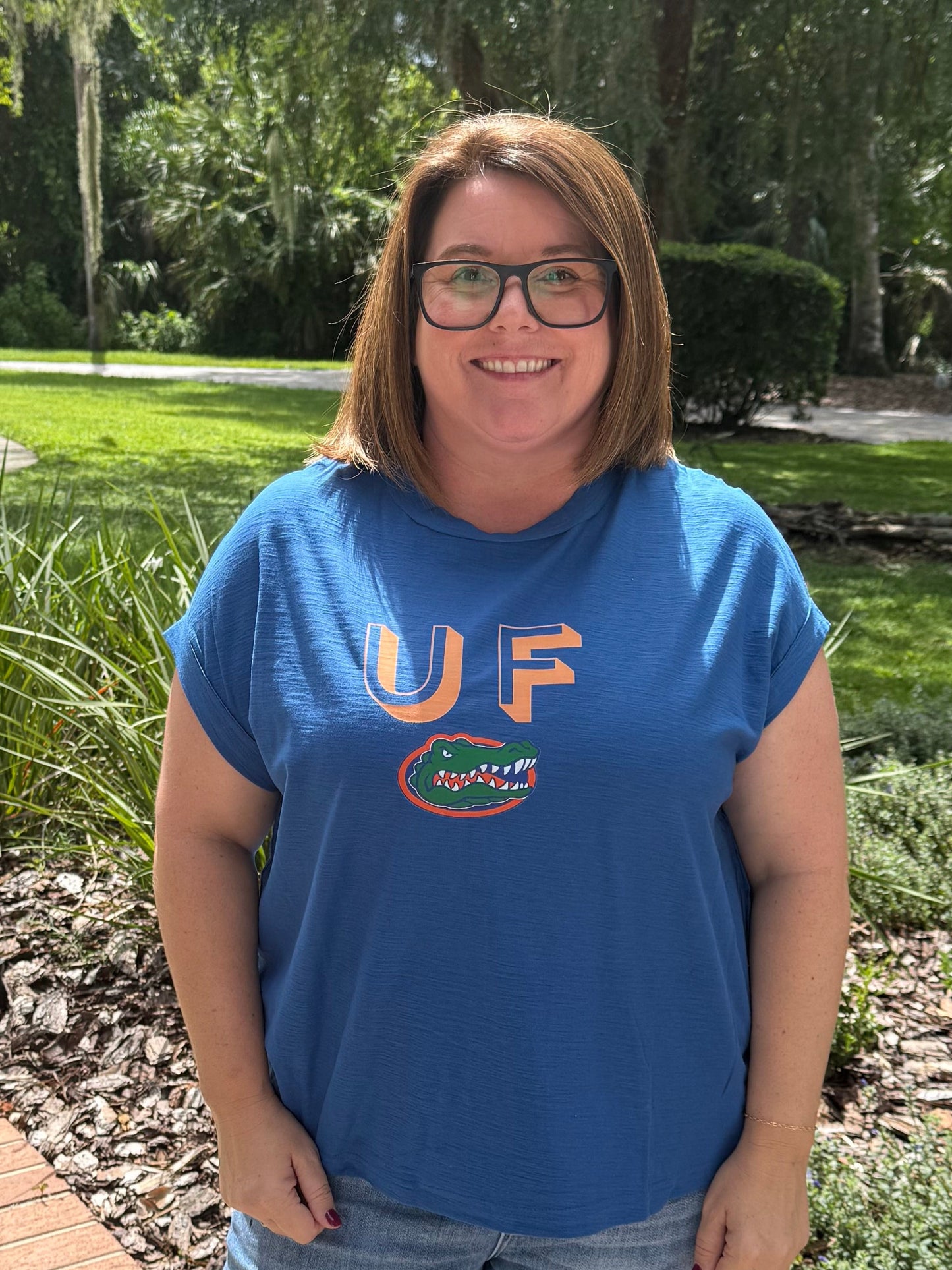 Person wearing a blue shirt with a logo, standing outdoors on a sidewalk.